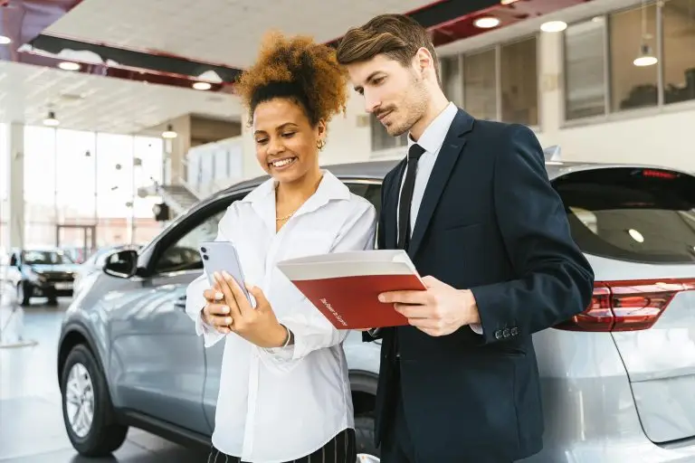 Man and woman standing in a car dealership looking at paperwork